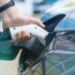 Hand plugging an EV charging connector into an electric car at a charging station