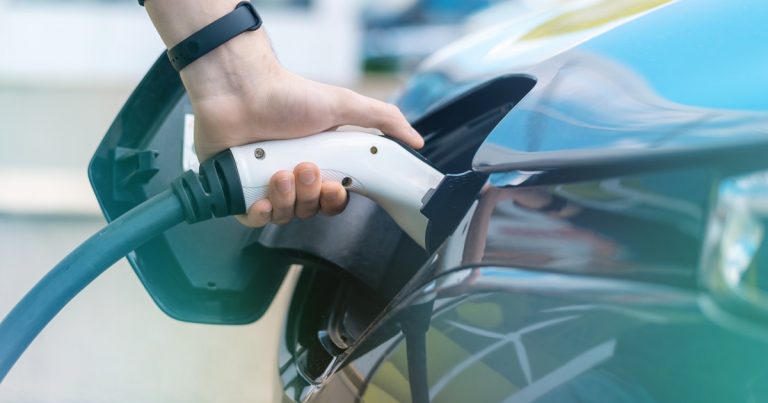 Hand plugging an EV charging connector into an electric car at a charging station