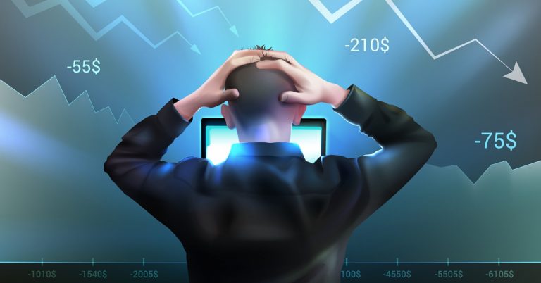 Stressed trader holding head while looking at computer as stock market charts fall and losses are shown on screen