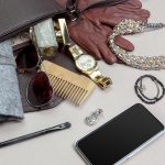 Contents of a women’s handbag including jewelry, watch, gloves, sunglasses, makeup brush, wallet and smartphone on table