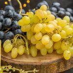 Fresh green and black grapes displayed on wooden board with Christmas decorations and festive lights in background