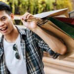 Smiling young man holding shopping bags outdoors, enjoying a retail shopping spree at a mall