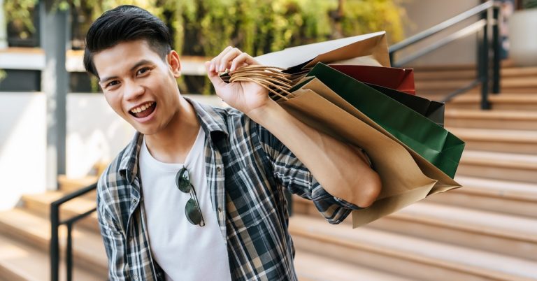 Smiling young man holding shopping bags outdoors, enjoying a retail shopping spree at a mall