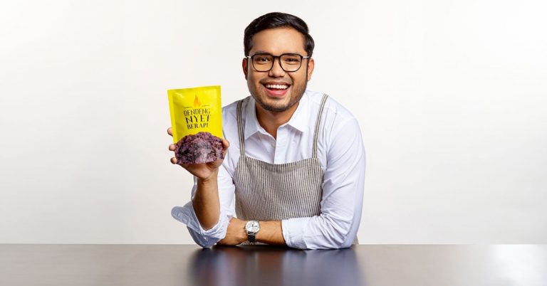 Smiling man holding a spicy beef jerky snack pack, presenting a Malaysian food product in a studio setting