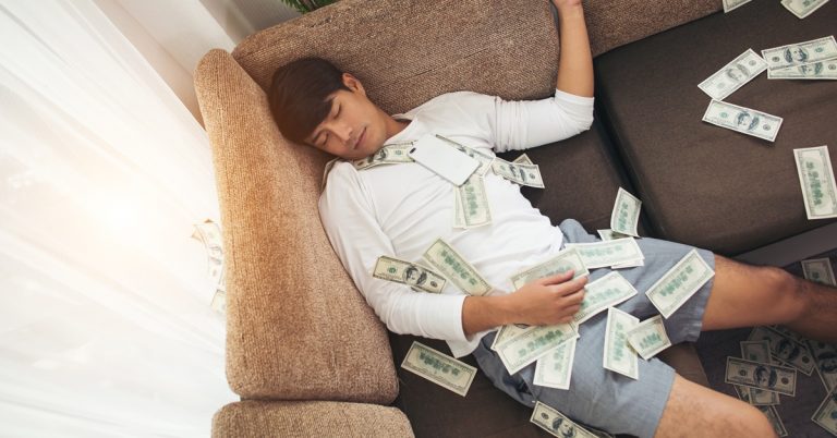 Man sleeping on sofa covered with dollar bills at home, symbolizing wealth, financial success or money windfall