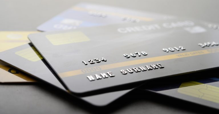 Close-up of stacked credit cards showing card numbers and names, representing payments, spending and personal finance