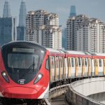 Red MRT train traveling on elevated tracks with Kuala Lumpur city skyline in the background, representing urban public transport