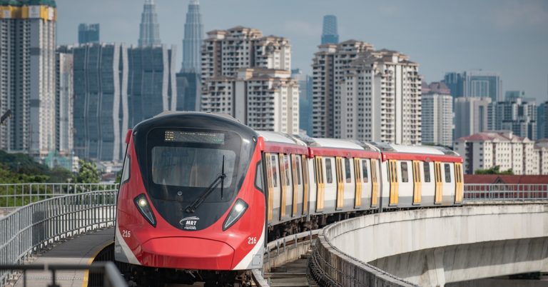 Red MRT train traveling on elevated tracks with Kuala Lumpur city skyline in the background, representing urban public transport