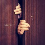 Hands gripping a slightly opened wooden closet door, symbolising hidden struggles, secrecy, or mental health awareness