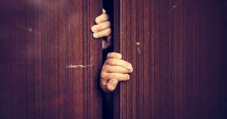 Hands gripping a slightly opened wooden closet door, symbolising hidden struggles, secrecy, or mental health awareness