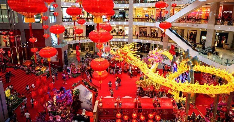 Shopping mall decorated for Chinese New Year with red lanterns, golden dragon display, festive crowd, and vibrant holiday atmosphere