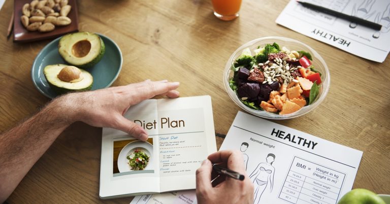 Person planning healthy diet with tablet, salad bowl, avocado, nuts and BMI chart on table, nutrition and weight loss concept