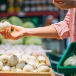 Woman selecting fresh onions at grocery store produce section while holding a shopping basket