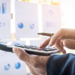 Business professional using calculator and pen with financial charts in background, budgeting and financial analysis concept