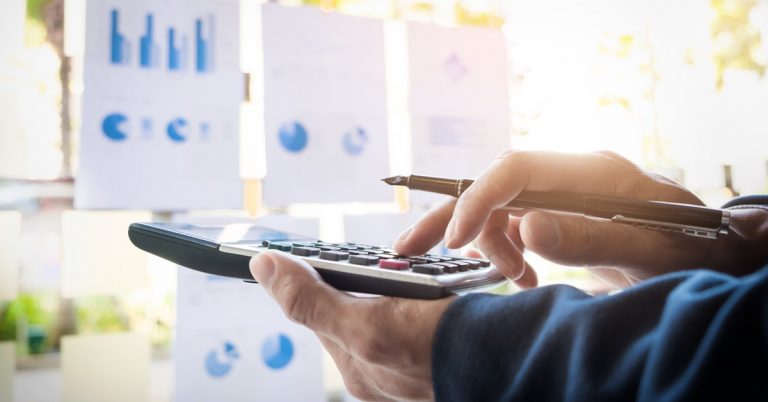 Business professional using calculator and pen with financial charts in background, budgeting and financial analysis concept