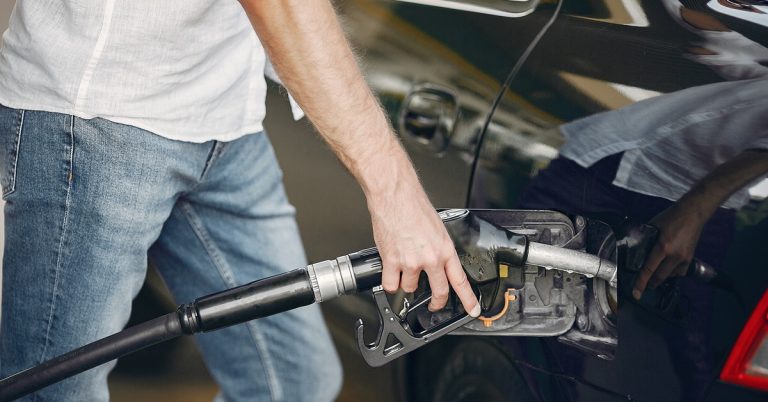 Man refueling car at petrol station with fuel pump nozzle, representing rising fuel costs and transportation expenses