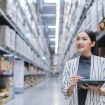 Asian woman using tablet to check inventory in warehouse, managing stock and logistics in distribution center