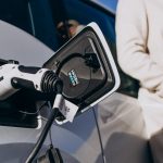 Woman charging electric car at home using EV charger plug with vehicle charging port close-up and modern lifestyle concept