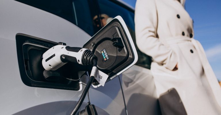 Woman charging electric car at home using EV charger plug with vehicle charging port close-up and modern lifestyle concept