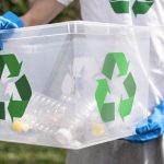 Person wearing gloves holding recycling bin with plastic bottles, promoting environmental cleanup and sustainable waste management