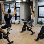Group indoor cycling class in gym with instructor and participants exercising on stationary bikes, promoting fitness and cardio workout