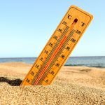 Thermometer in beach sand showing high temperature near ocean, symbolizing heatwave, summer weather and climate change