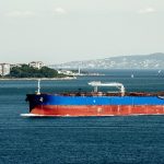 Cargo tanker ship sailing on blue sea near coastal city, representing maritime transport, shipping industry and global trade