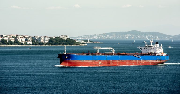 Cargo tanker ship sailing on blue sea near coastal city, representing maritime transport, shipping industry and global trade