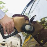 Person refueling car at gas station with fuel pump nozzle, representing petrol prices, transportation and vehicle costs
