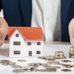 Hands protecting a model house with coins, symbolising home loan protection and financial security
