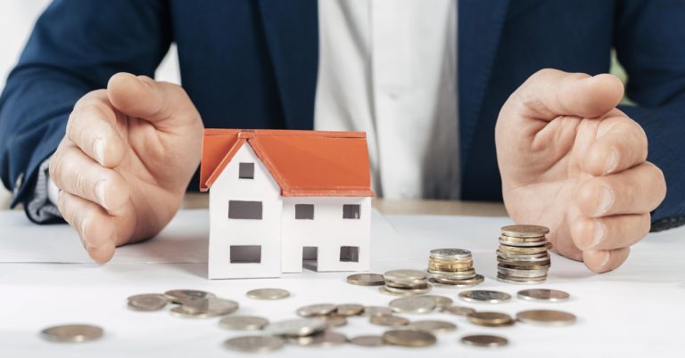 Hands protecting a model house with coins, symbolising home loan protection and financial security
