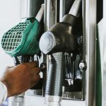 Person holding fuel pump nozzle at petrol station, symbolizing fuel prices, refueling costs and transportation expenses