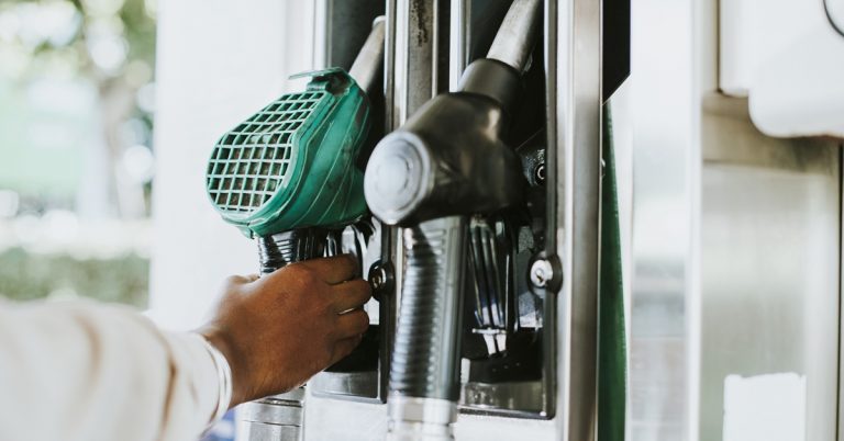 Person holding fuel pump nozzle at petrol station, symbolizing fuel prices, refueling costs and transportation expenses
