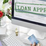 Loan approved application displayed on computer screen with customer holding credit card for personal financing approval