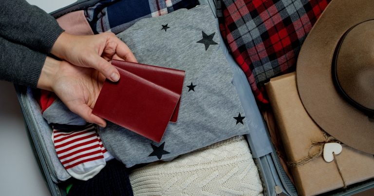 Woman hands with passports on the background open suitcase packed for travelling.