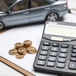 Model car, calculator, and coins on clipboard representing car loan and vehicle ownership cost calculations