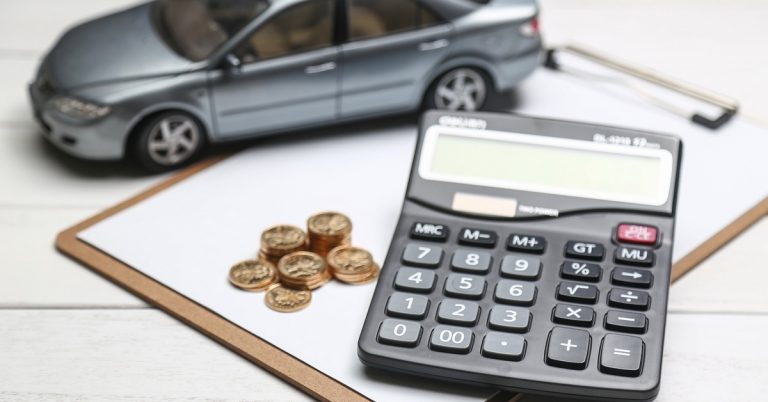 Model car, calculator, and coins on clipboard representing car loan and vehicle ownership cost calculations