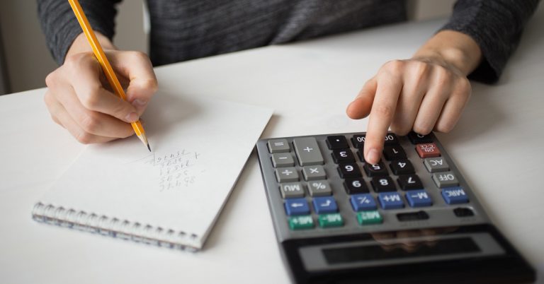 Person using a calculator and writing financial calculations in a notebook for budgeting, accounting, tax planning, or personal finance management.